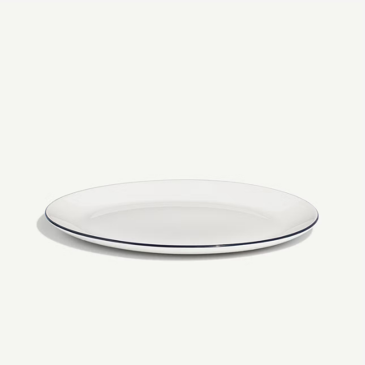 A white oval serving platter with a thin dark blue rim, photographed on a clean off-white background.