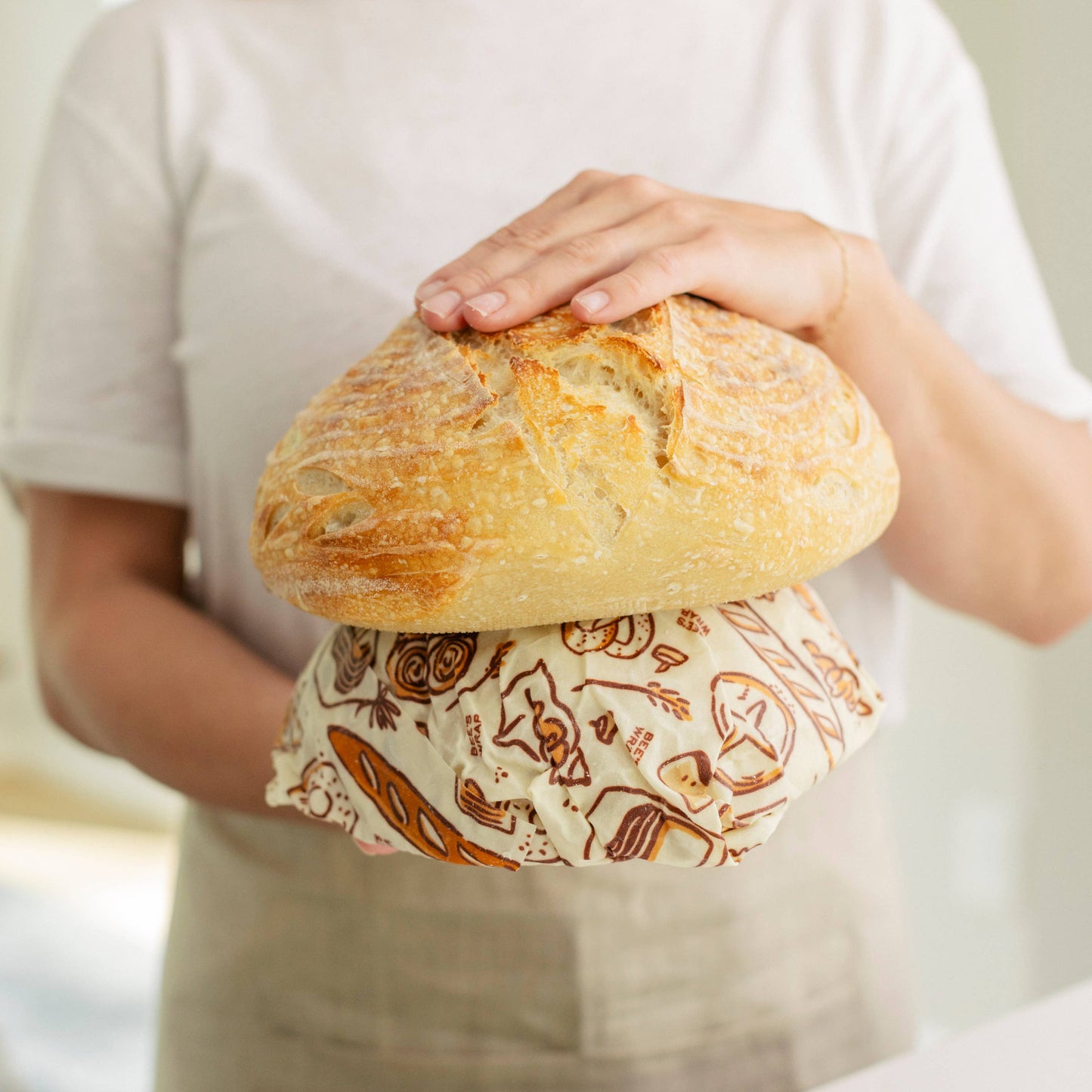 Person holding a loaf of bread wrapped in a patterned paper bag.