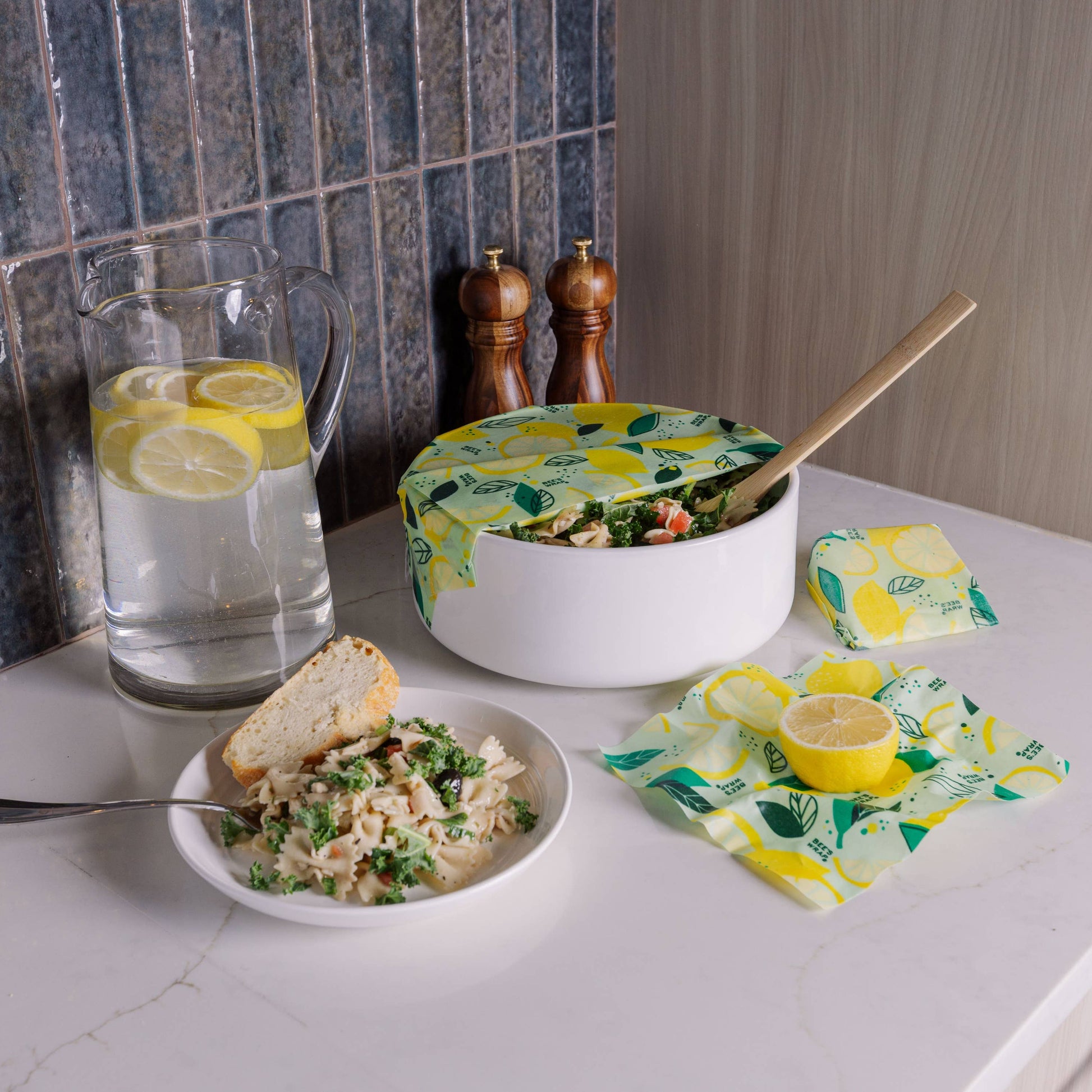 Kitchen counter with a bowl of salad, a glass of water with lemon slices, and a pot with a lid on a countertop.