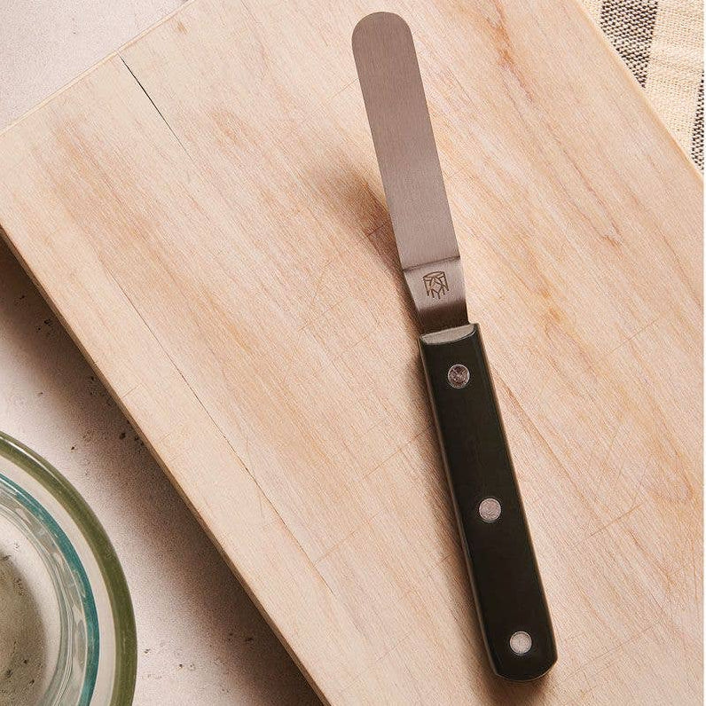 Spreader knife with black handle on a wooden cutting board