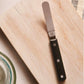 Butter knife on a wooden cutting board with a striped cloth in the background