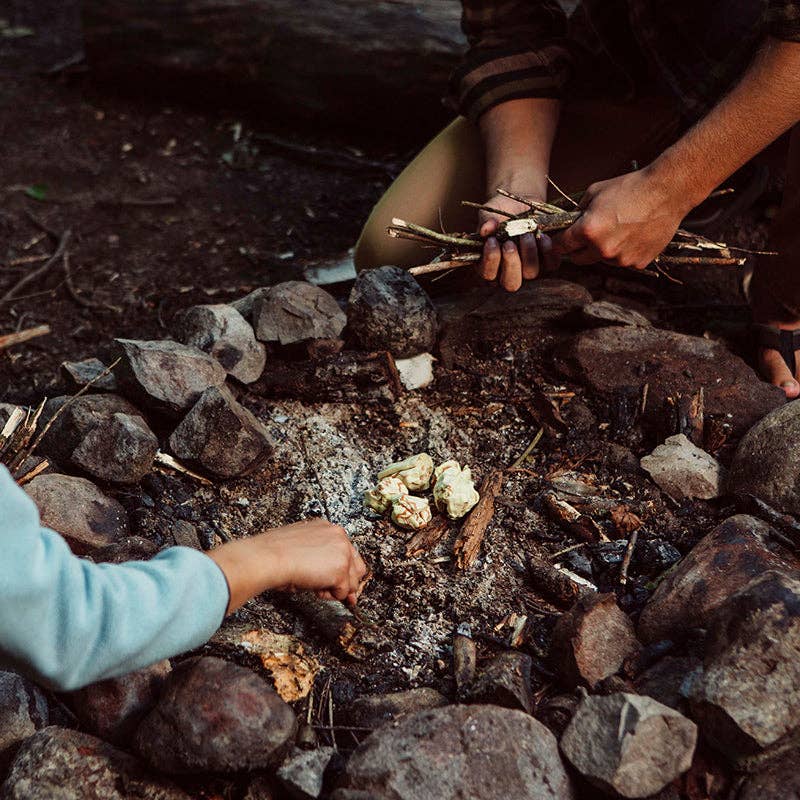 Two people building a fire with sticks on a rocky ground.