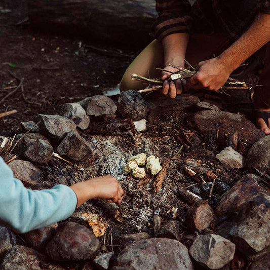 Two people building a fire with sticks on a rocky ground.