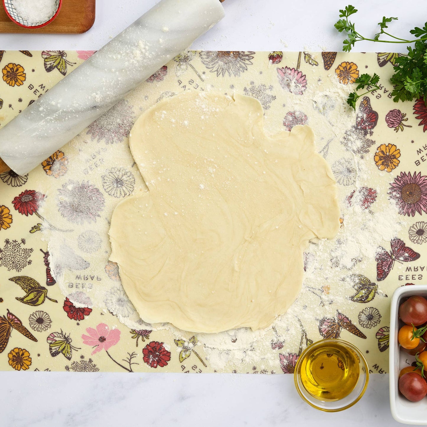 Flourished dough with a rolling pin on a decorative mat, surrounded by ingredients.