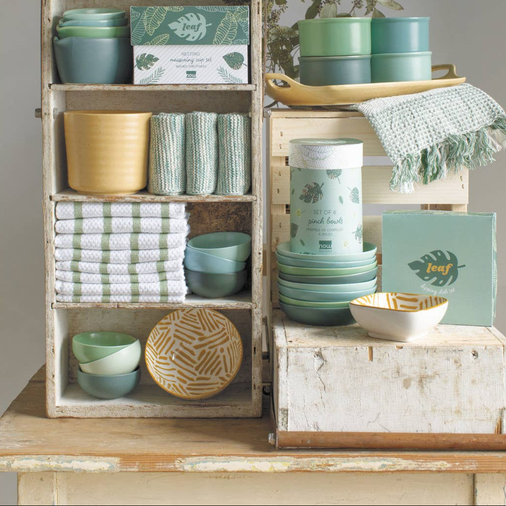 Display of green kitchenware including bowls, cups, and a towel on a wooden shelf.