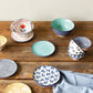 Collection of patterned ceramic plates and bowls on a wooden surface with a gray sweater.