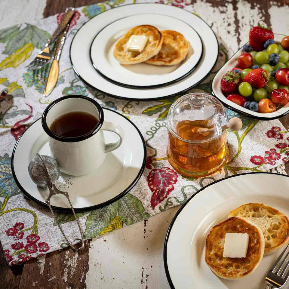 Breakfast setting with crumpets, tea, coffee, and fruit on a wooden table.
