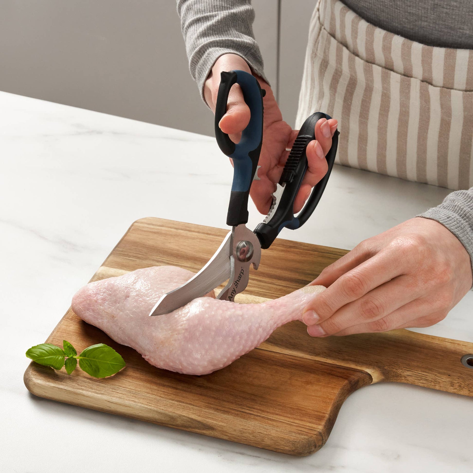 Person using kitchen shears to cut a chicken leg on a wooden cutting board.