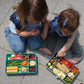 Two children sitting on a sidewalk with bento boxes filled with various food items.