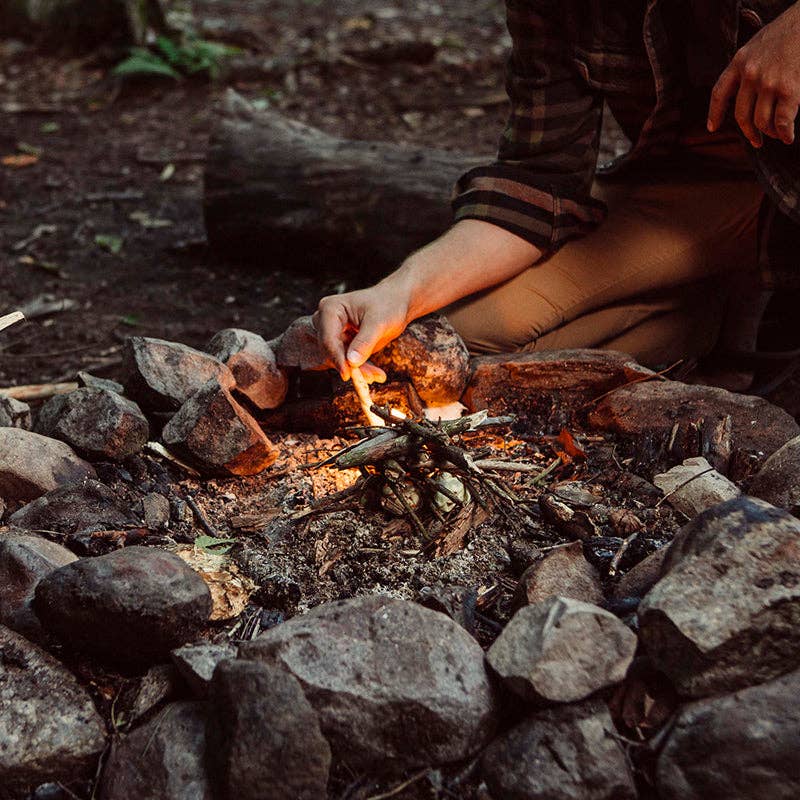 Person lighting a campfire with stones surrounding it in a natural setting