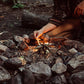 Person lighting a campfire with stones surrounding it in a natural setting