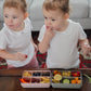 Children are sitting at a table with six-compartment food containers.