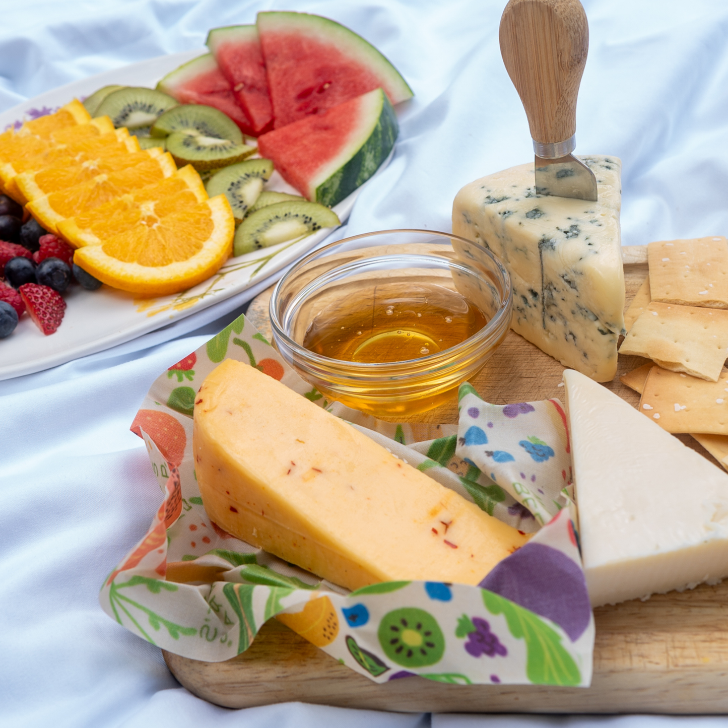 Cheese platter with fruits, honey, and crackers on a white cloth background