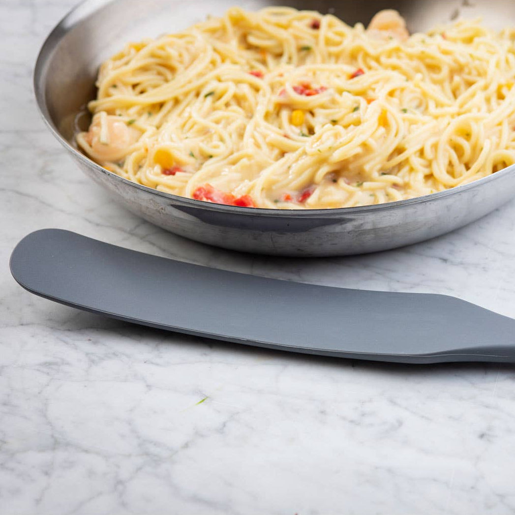 Frying pan with pasta dish on a marble surface next to a gray spatula