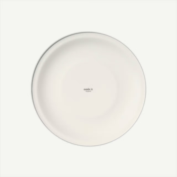 A minimalist white ceramic plate photographed from directly above on a clean, off-white background. The plate features a small printed text in the center reading 'made in Germany'.