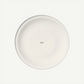 A minimalist white ceramic plate photographed from directly above on a clean, off-white background. The plate features a small printed text in the center reading 'made in Germany'.