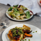 Plated dish with roasted chicken and vegetables on a table with a salad in the background.