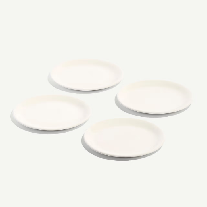 Four plain white ceramic plates of varying sizes arranged in a loose square on a very light off-white background.