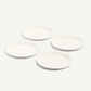 Four plain white ceramic plates of varying sizes arranged in a loose square on a very light off-white background.
