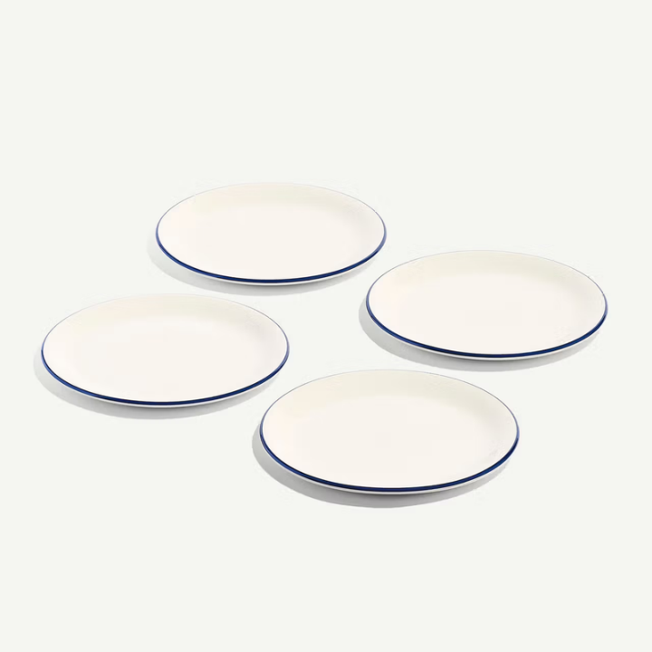 Four white oval plates with thin blue rims, arranged in a loose square on a clean off-white background.
