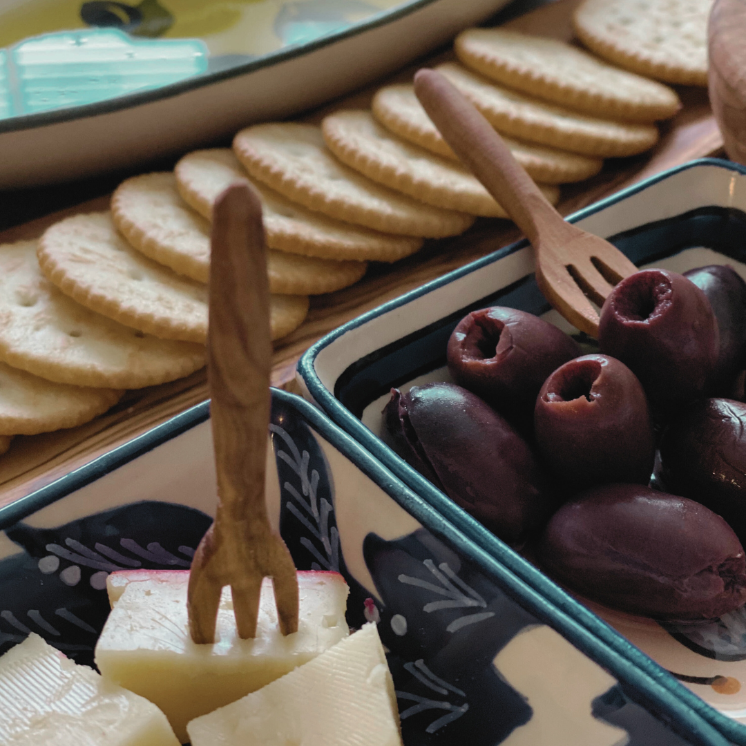 olive wood appetizer fork being used on a charcuterie board with cheese and olives