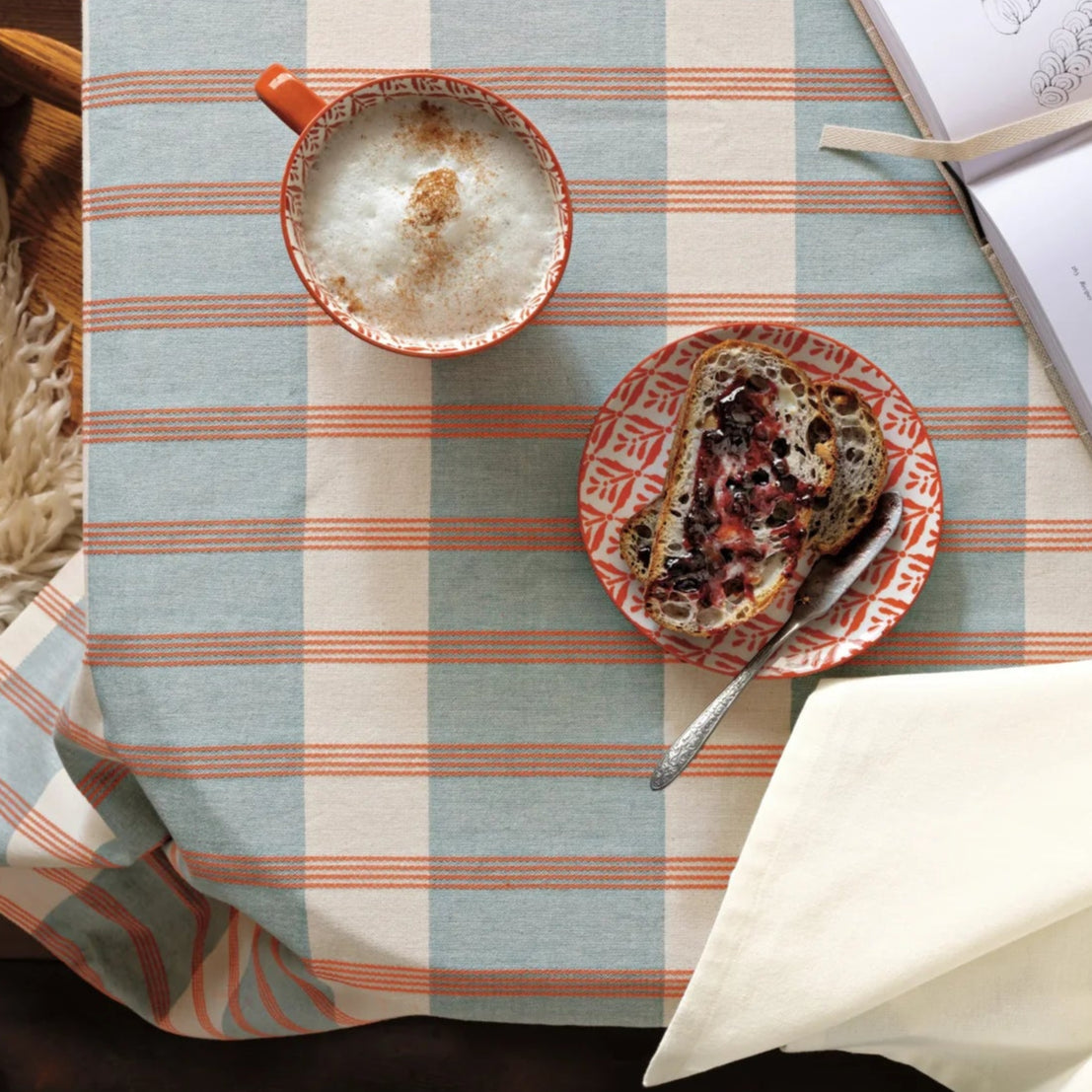 Table setting with a mug, plate of food, and book on a striped tablecloth.