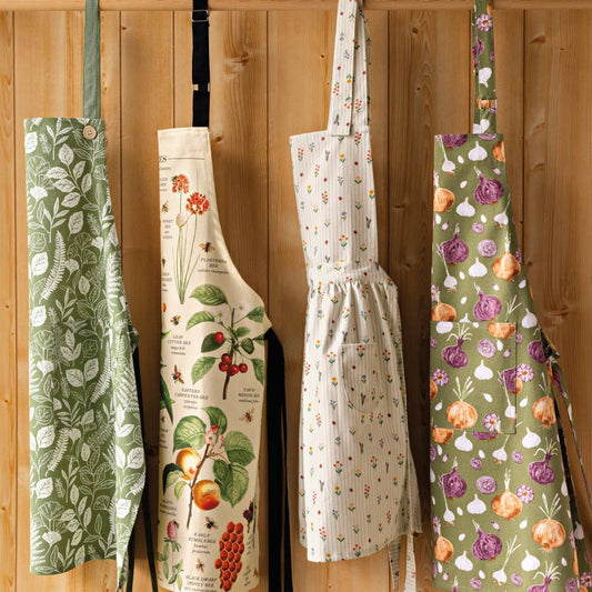 Four aprons with floral and nature-themed designs hanging on a wooden wall.
