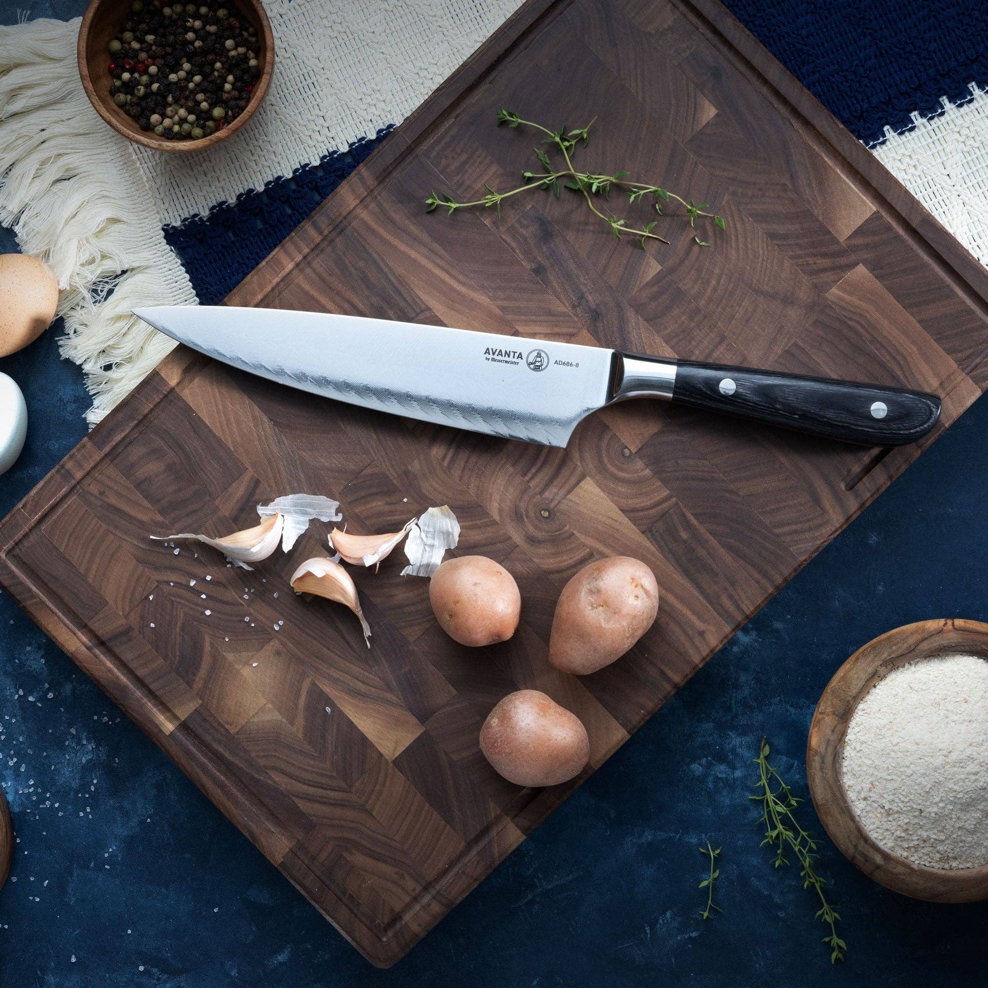 Knife on wood cutting board with garlic, potatoes, and spices on a blue surface