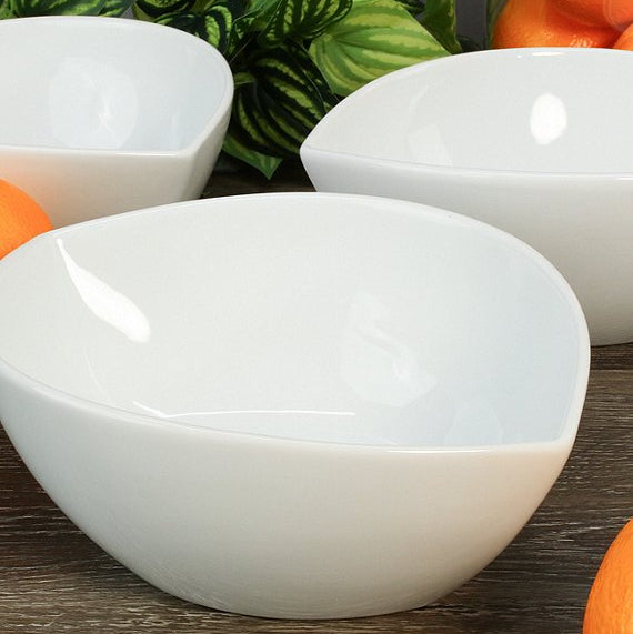 White ceramic bowls on a wooden surface with green leaves and oranges in the background
