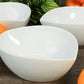 White ceramic bowls on a wooden surface with green leaves and oranges in the background