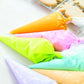 Colorful piping bags filled with icing on a white surface with cookies in the background.