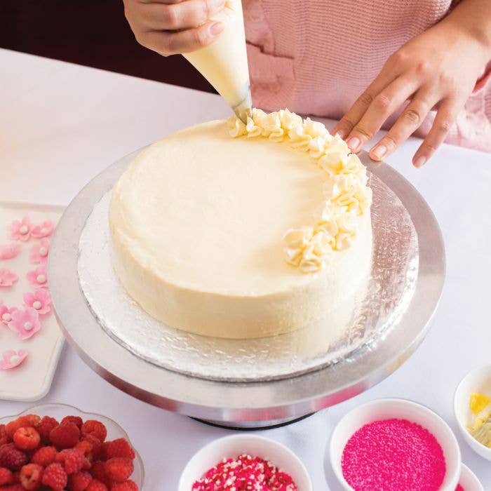 Person decorating a cake with white frosting on a white surface.