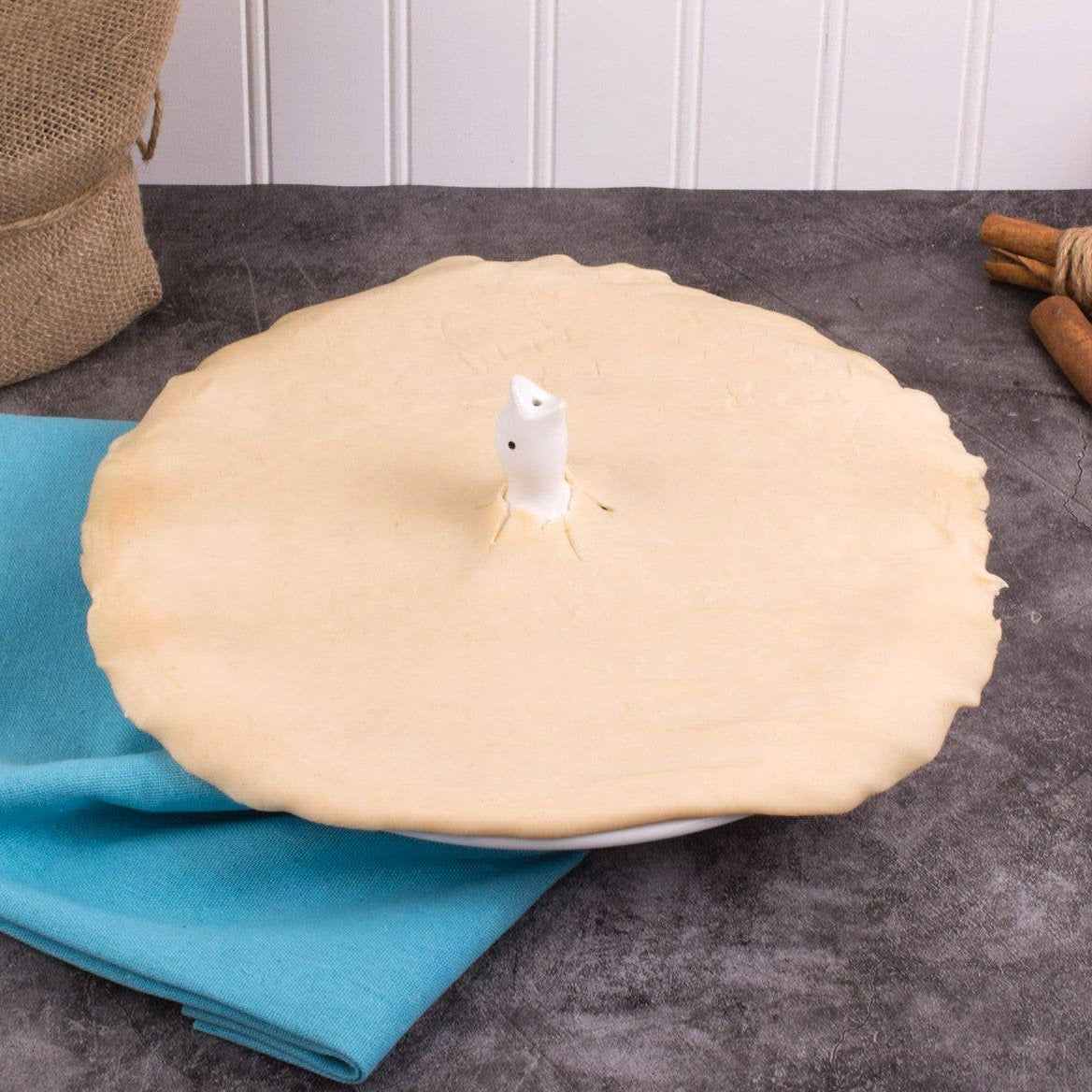 Pie with a Baking Pie Bird on a table with a blue cloth and cinnamon sticks.