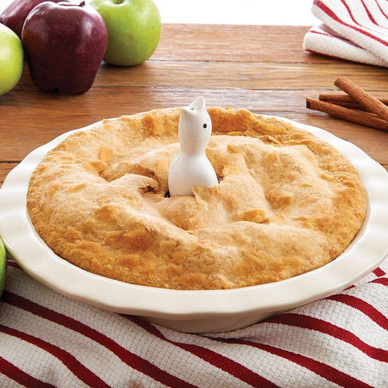 Pie with a pie bird, surrounded by apples and cinnamon sticks on a wooden table.
