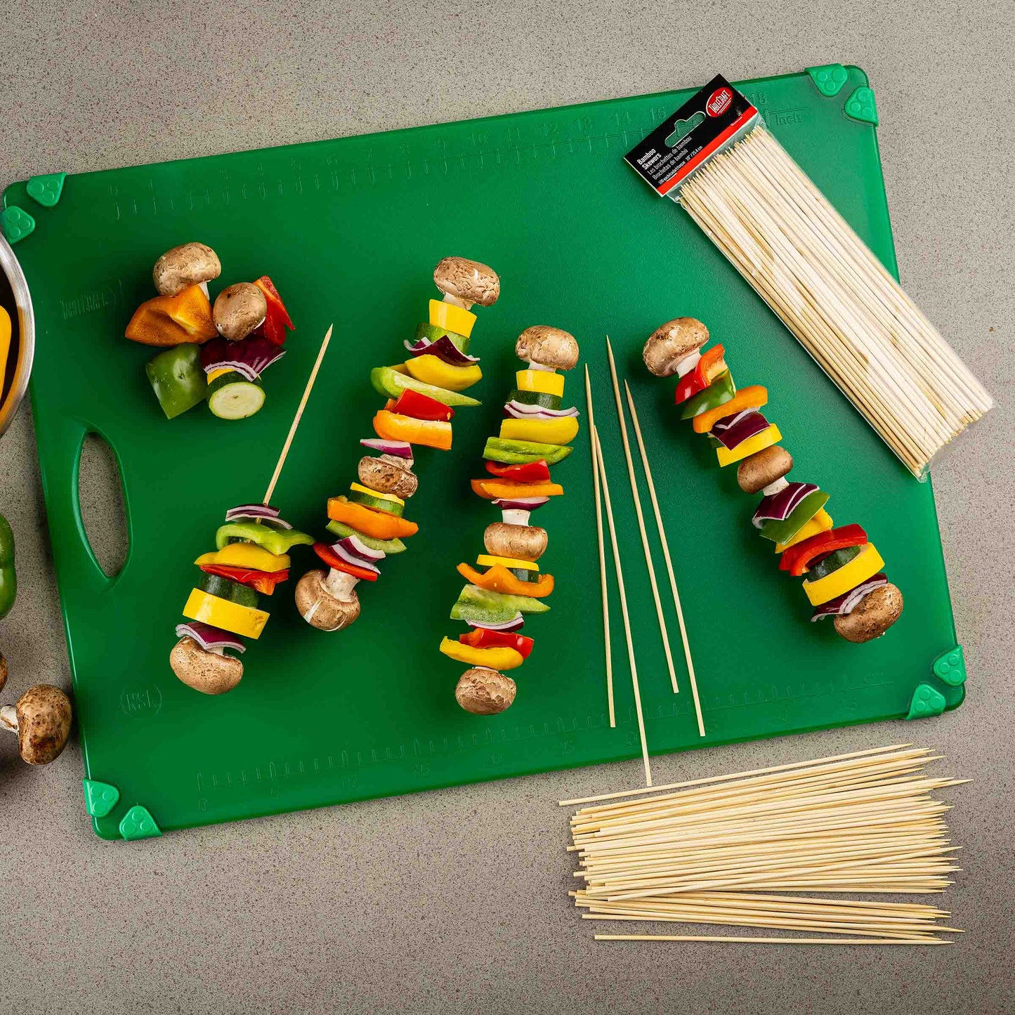 Colorful vegetable skewers on a green cutting board with additional skewers and packaging.