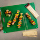 Colorful vegetable skewers on a green cutting board with additional skewers and packaging.