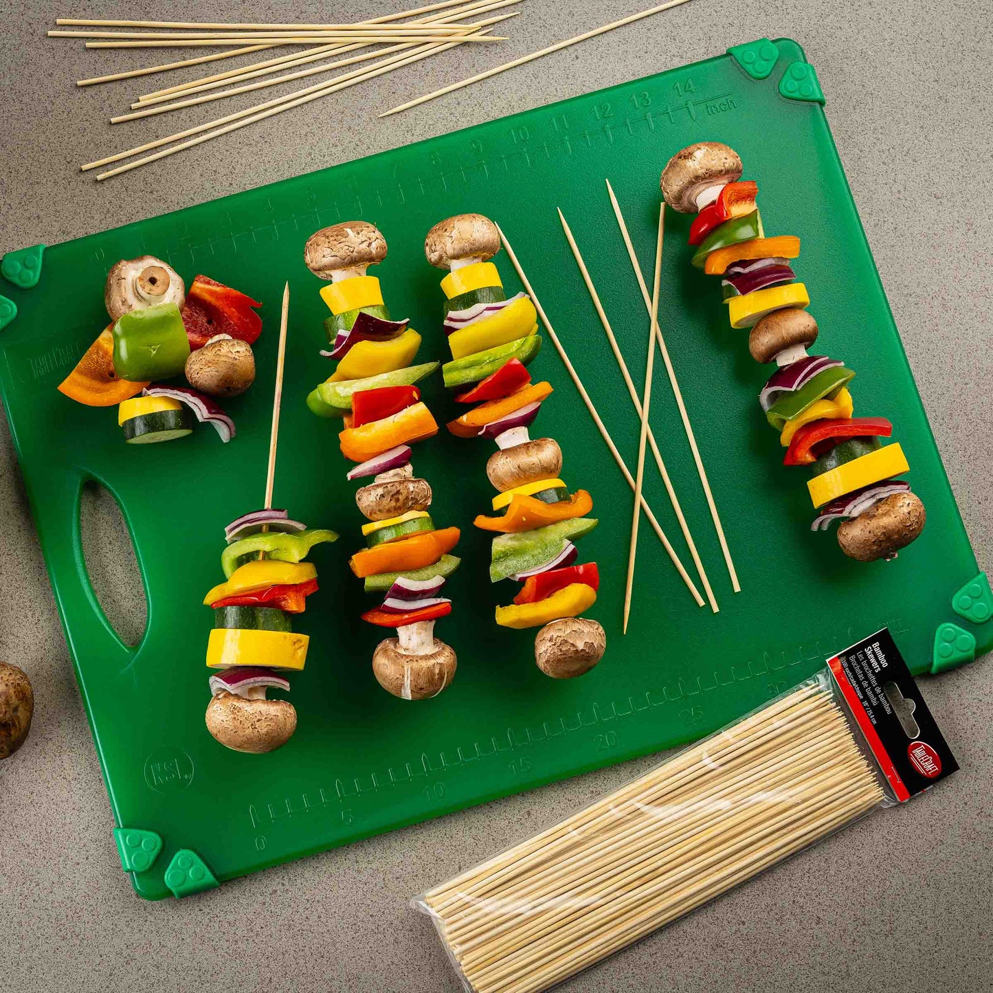 Colorful vegetable skewers on a green cutting board with wooden skewers and a package of additional skewers.