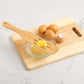 Wooden egg separator on a cutting board with eggs and a bowl of separated yolk.