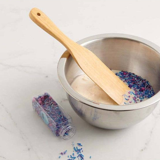 Metal bowl with wooden spurtle and colorful sprinkles on a marble surface