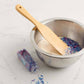 Metal bowl with wooden spurtle and colorful sprinkles on a marble surface