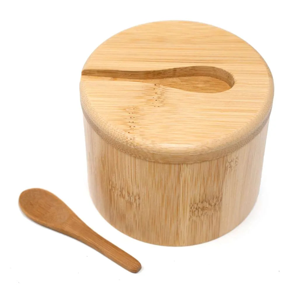 A round bamboo container with a matching lid featuring a cutout for a small wooden spoon, shown alongside a separate wooden spoon on a white background.