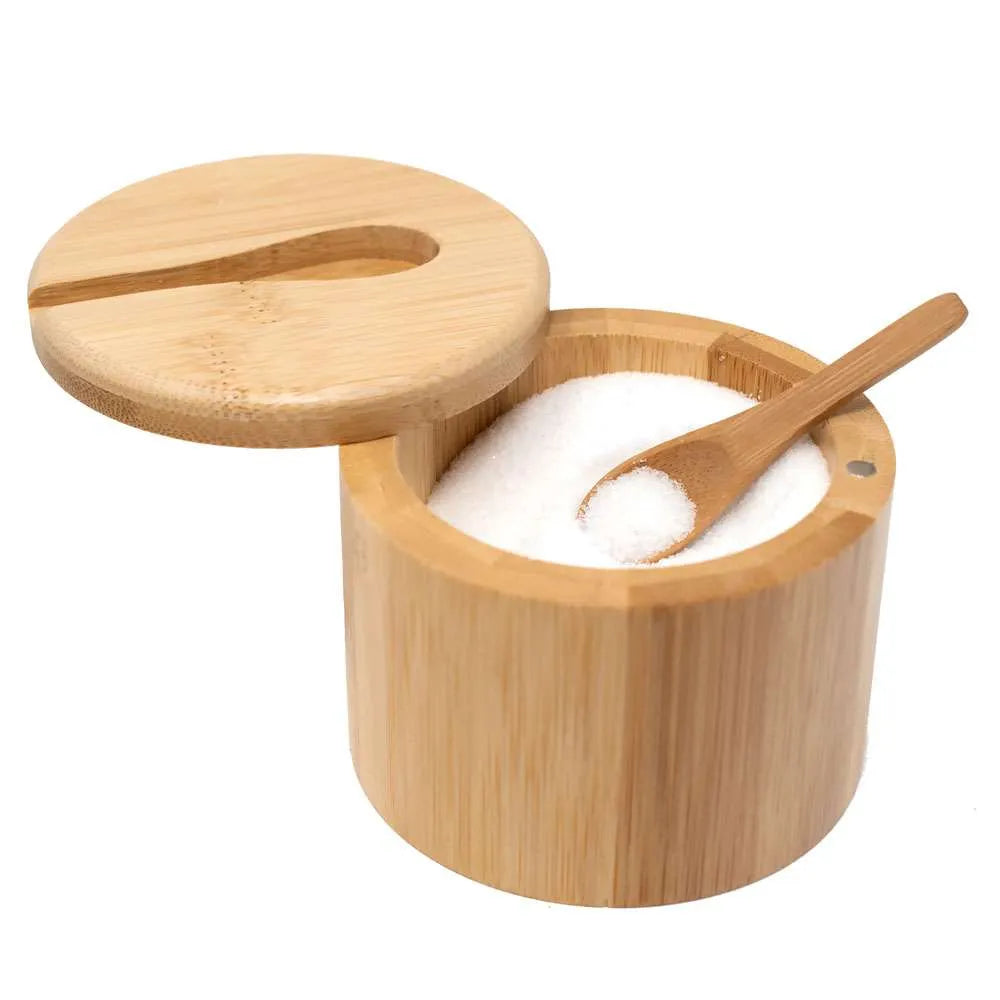 A round bamboo salt container with its lid off, filled with white salt and a small wooden spoon resting inside, shown on a plain white background.