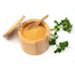 A light natural bamboo cylindrical spice container open, with yellow-orange ground spice and a small wooden spoon, with parsley on a white background.