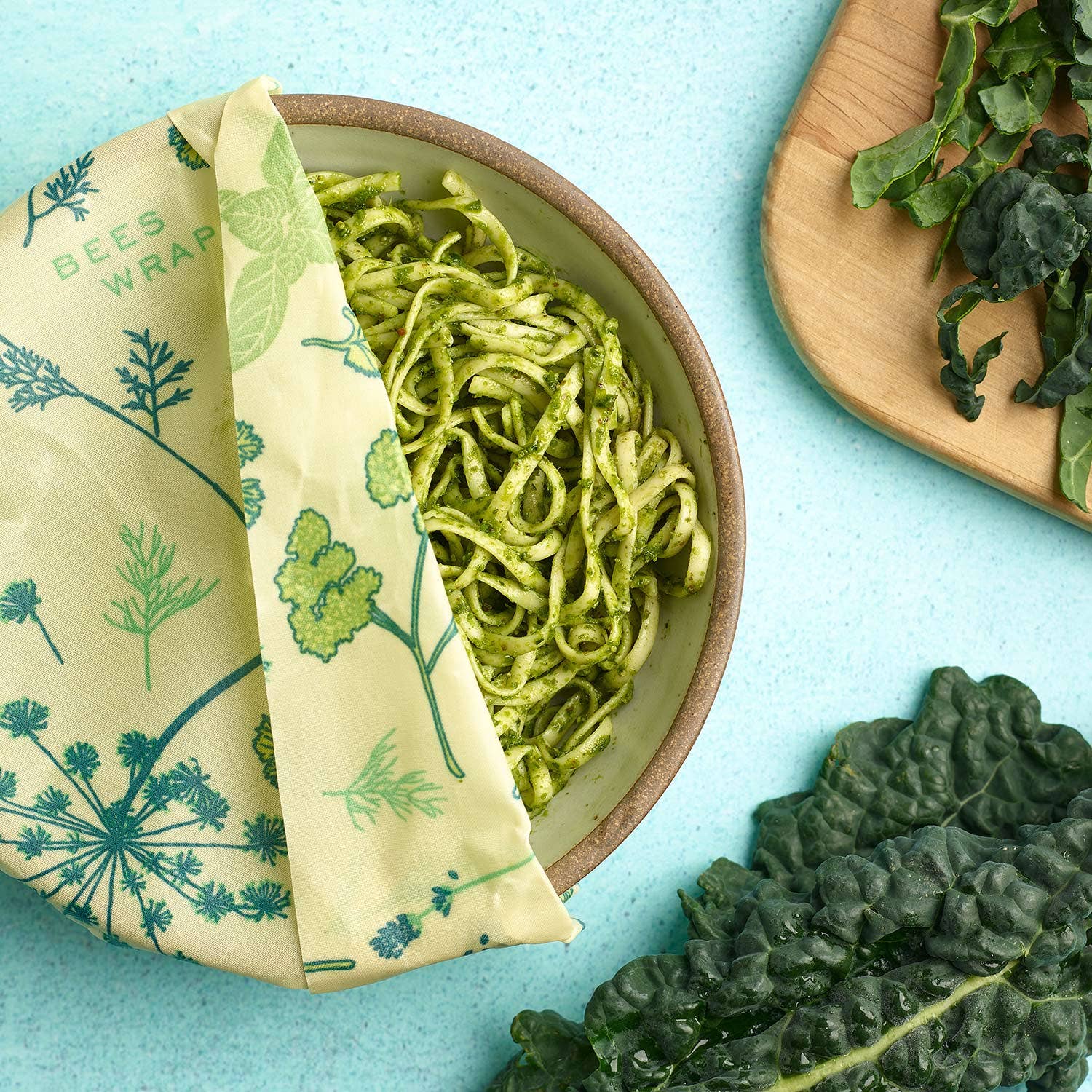 Beeswax wrap with a green leaf pattern on a blue background, used to wrap green pasta.
