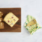 Wooden board with crackers and cheese, next to a reusable beeswax wrap on a white background