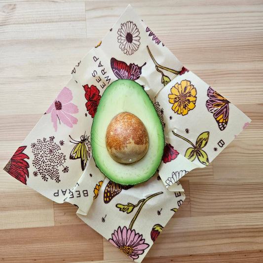 Half-cut avocado on a floral-patterned beeswax wrap on a wooden surface