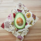 Half-cut avocado on a floral-patterned beeswax wrap on a wooden surface