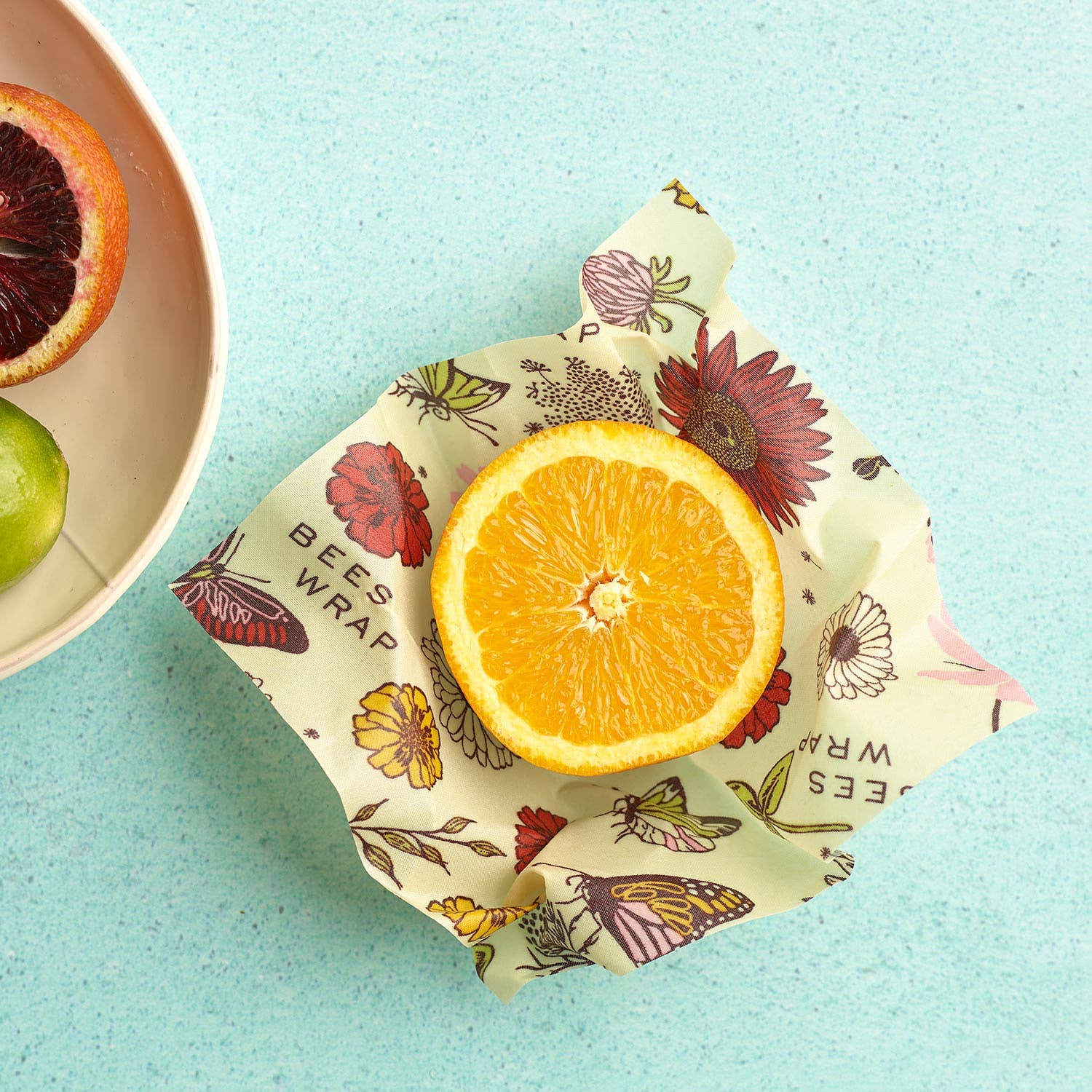 Half of an orange wrapped in a floral beeswax wrap on a light blue background