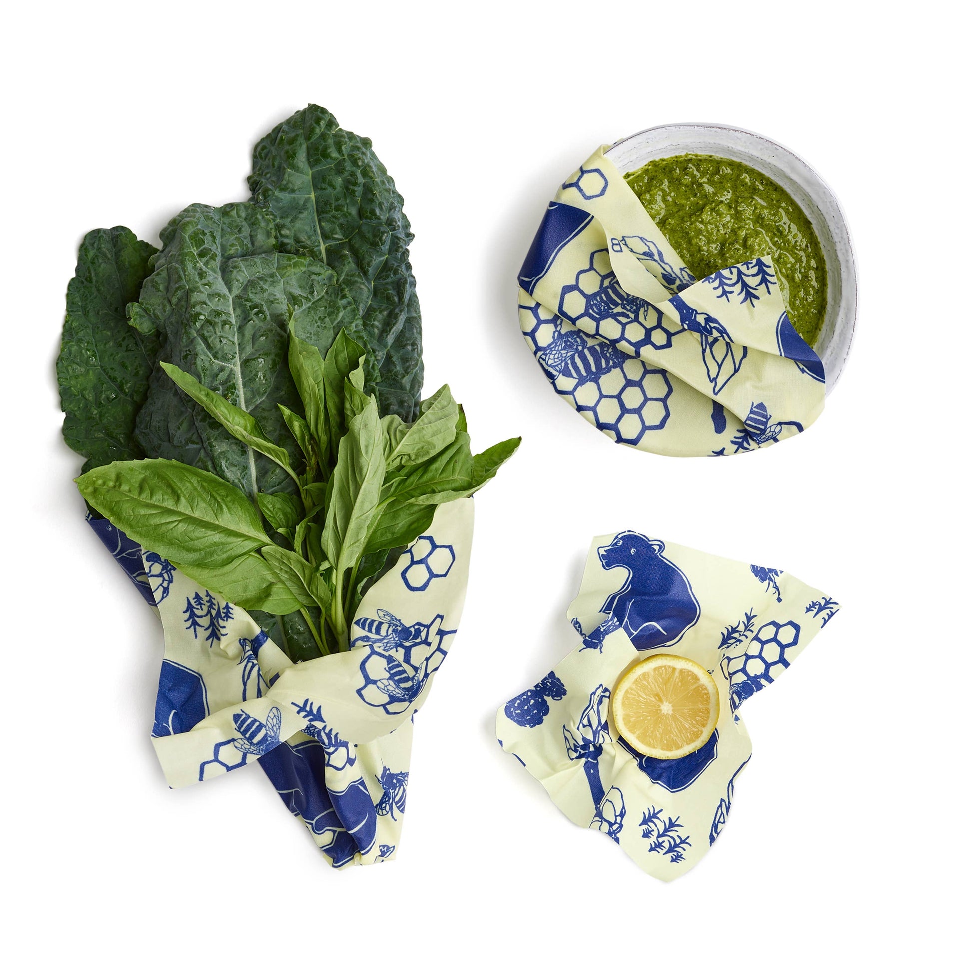 Reusable beeswax wraps with greens and a lemon on a white background
