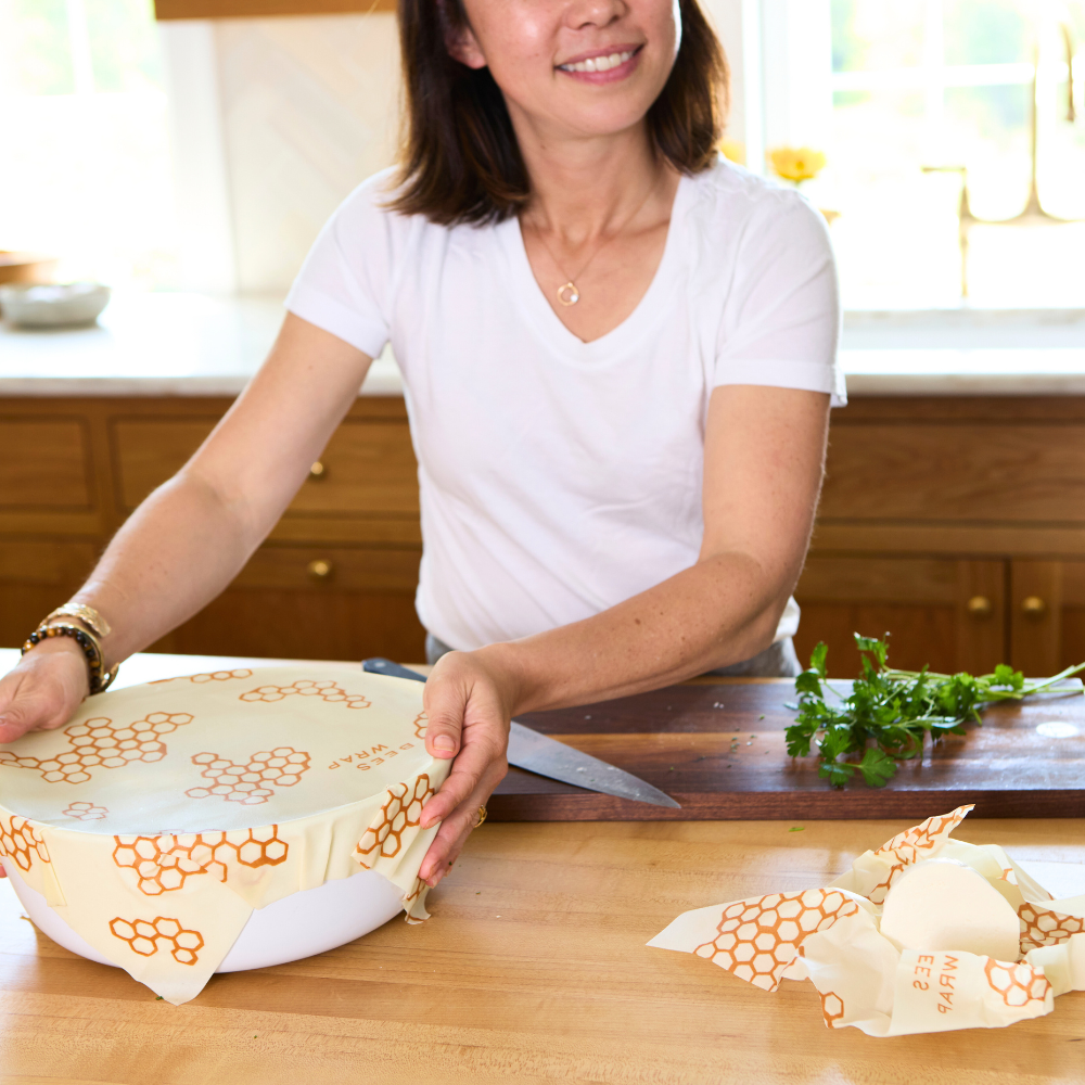Woman in a kitchen using beeswax food wrap on a wooden cutting board.